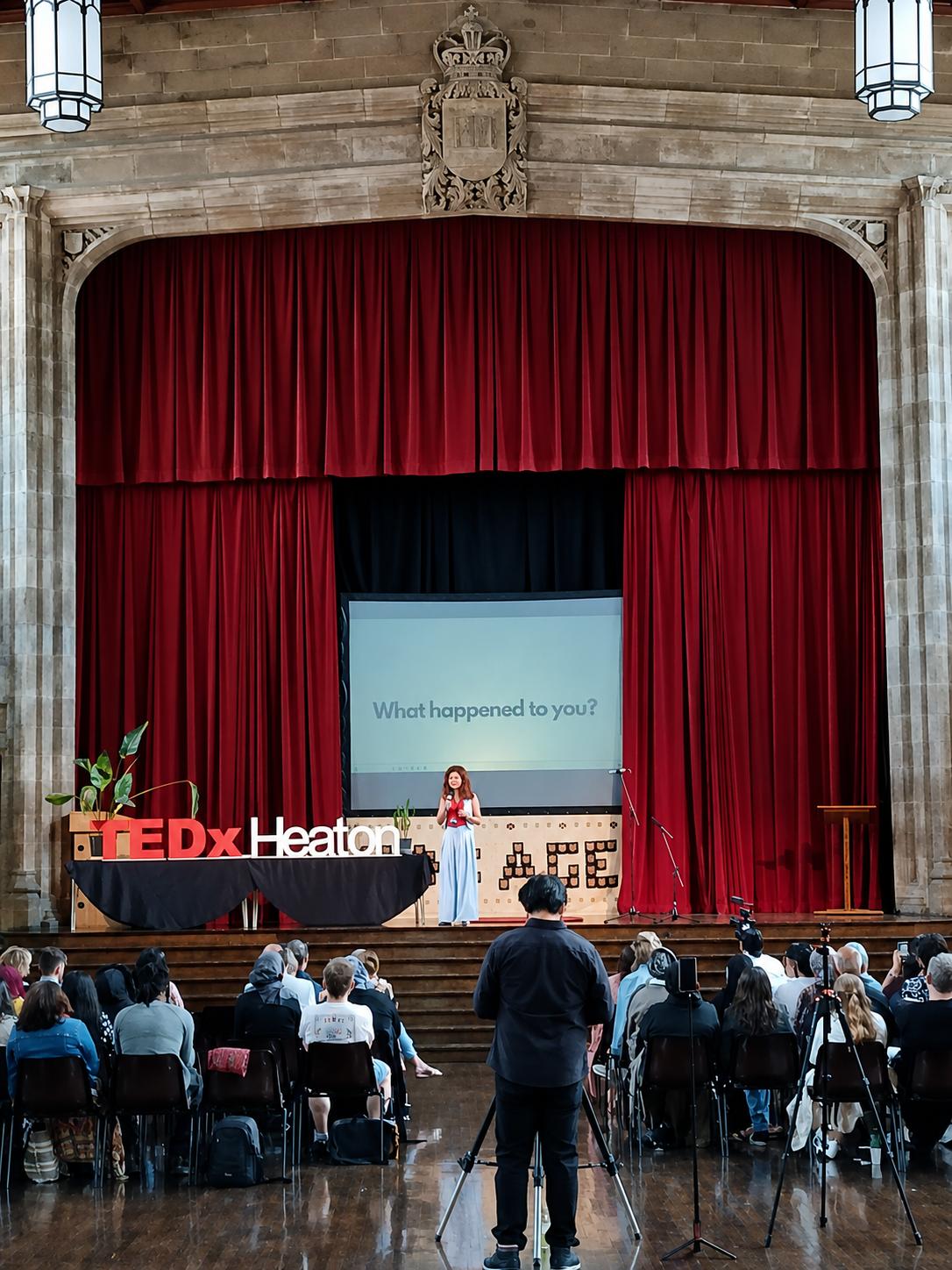 Adriana Welham presenting at TEDxHeaton, slide reading 'What happened to you?'